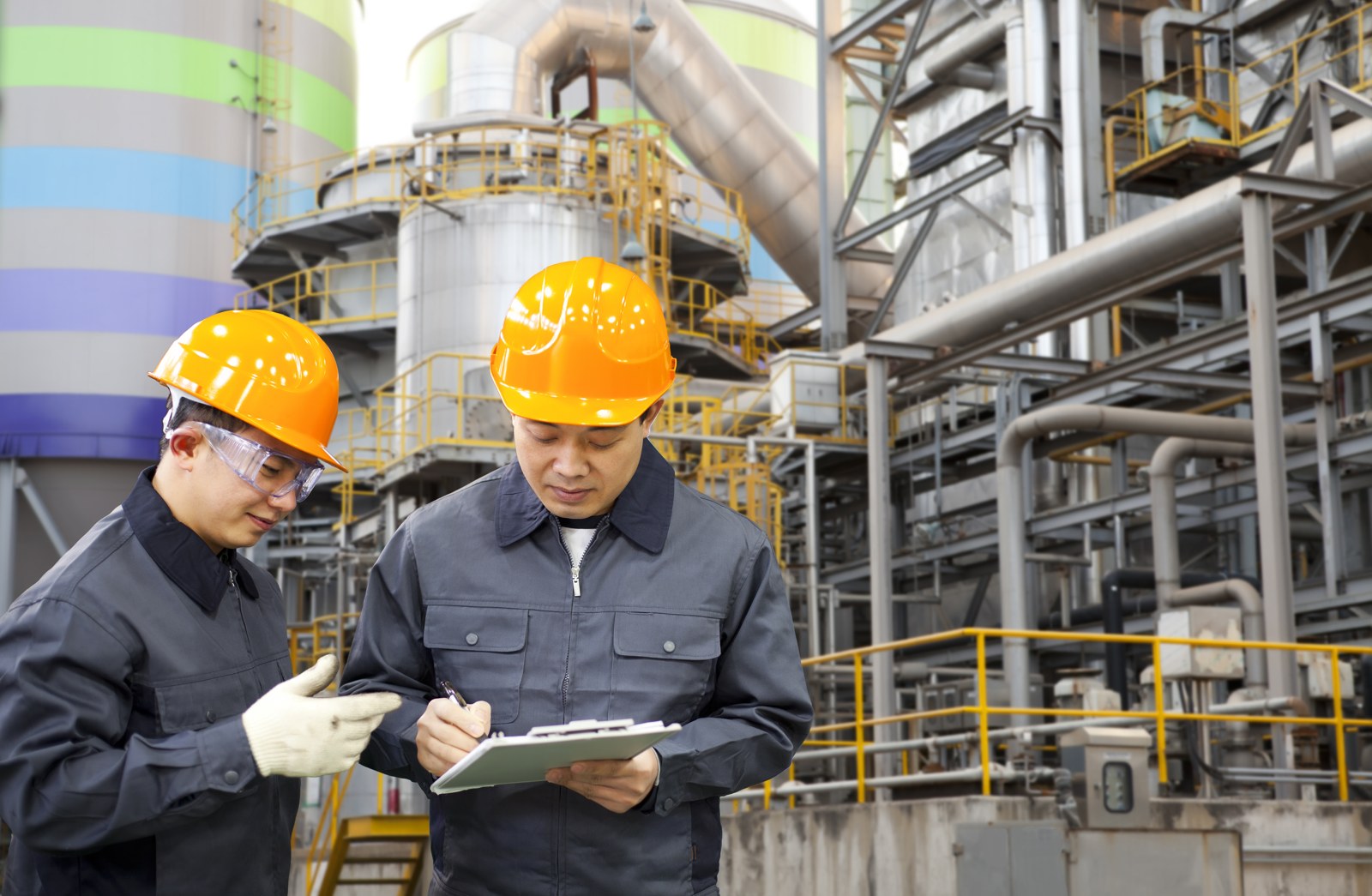 Two workers in hard hats reviewing records at an industrial plant
